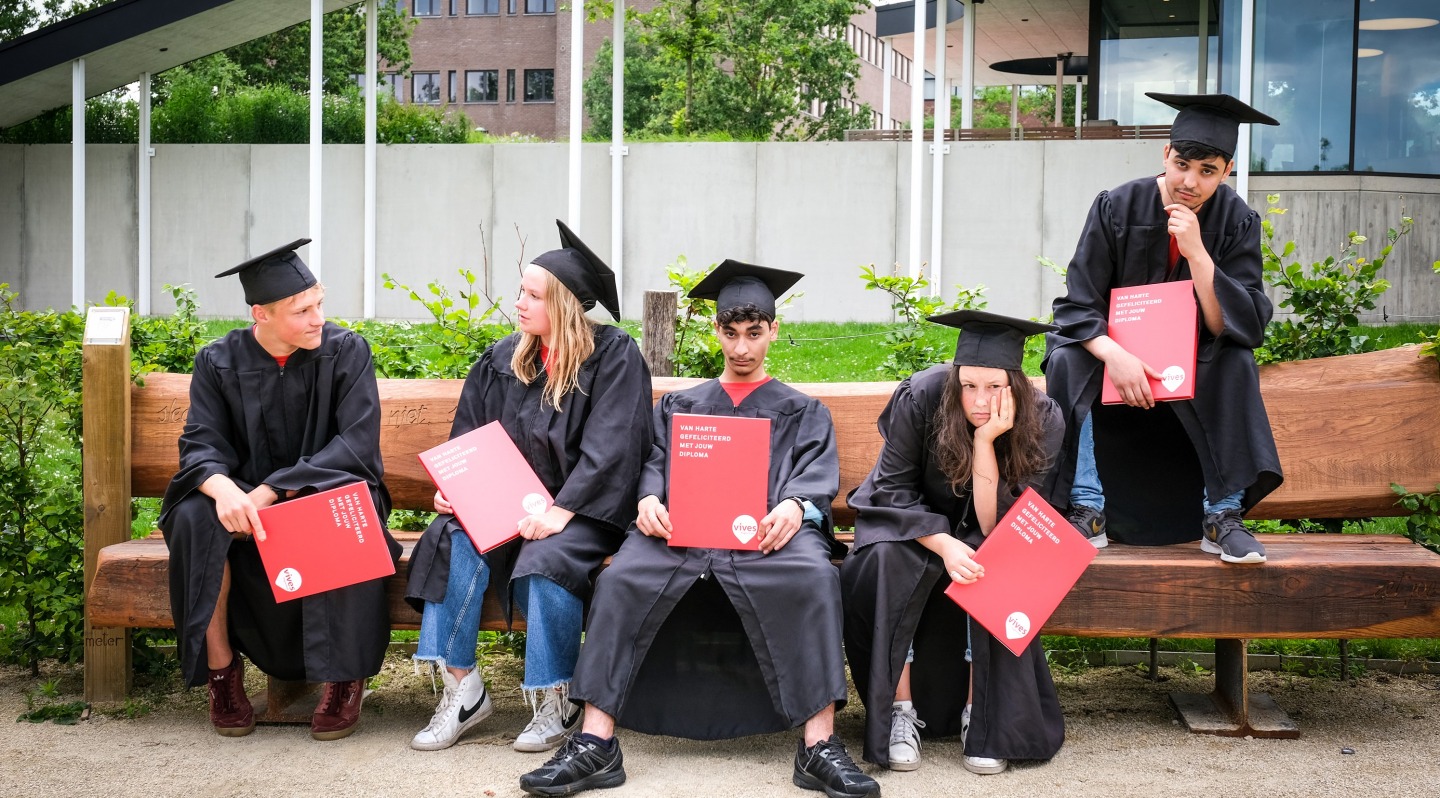 studenten VIVES Hogeschool zitten op een bankje met hun diploma in afstudeertoga